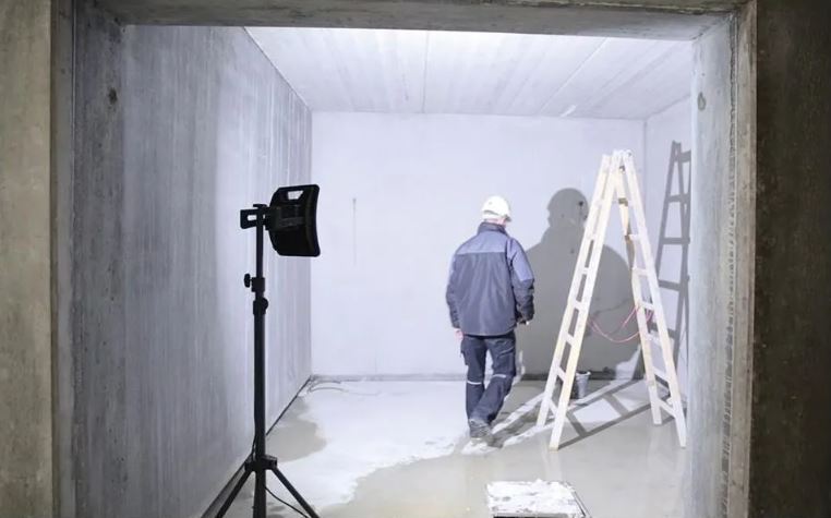 Een bouwlamp verlicht een onafgewerkte ruimte met een bouwvakker en een ladder.